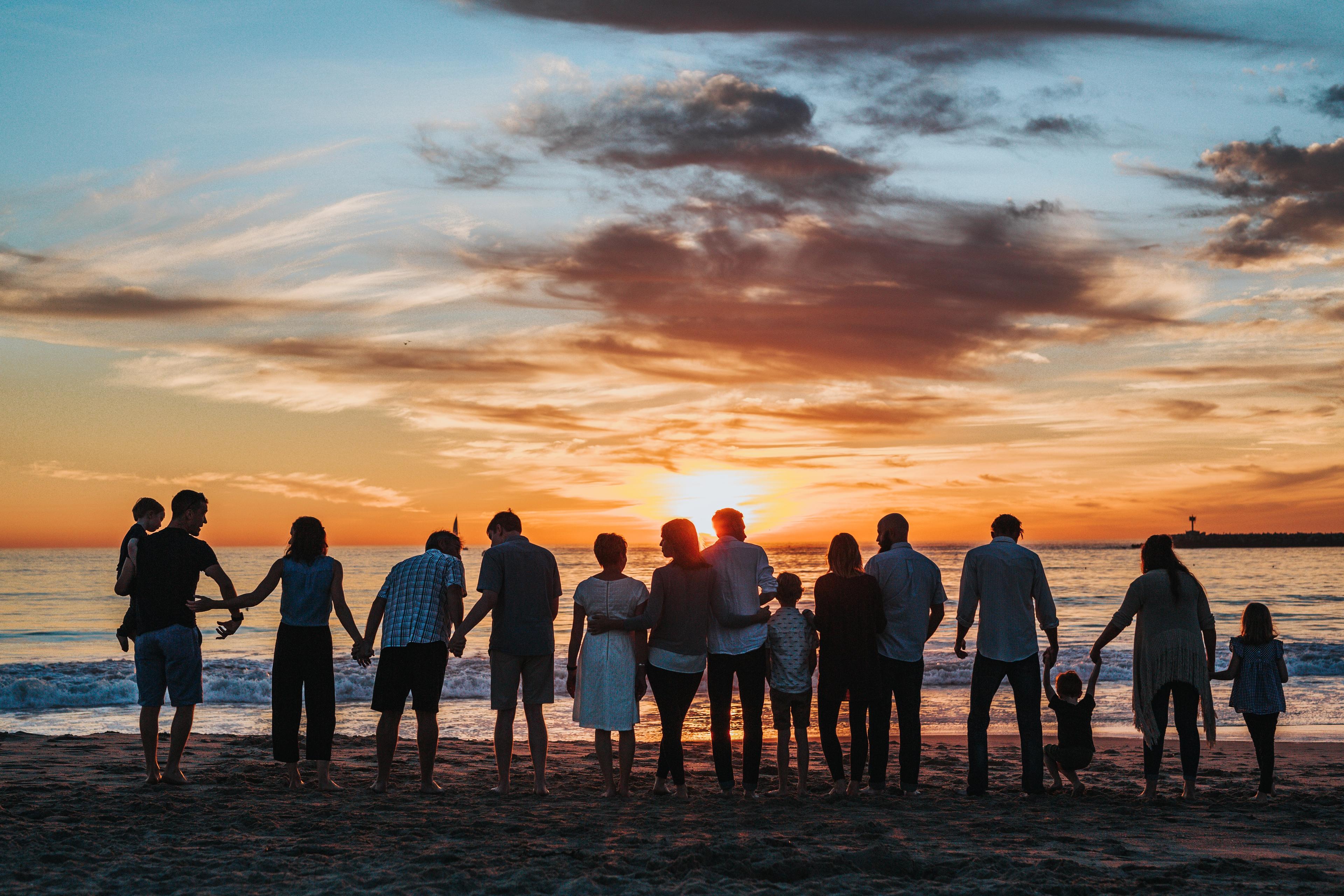 people looking towards the sunset on a shoreline where waves are almost hitting their legs